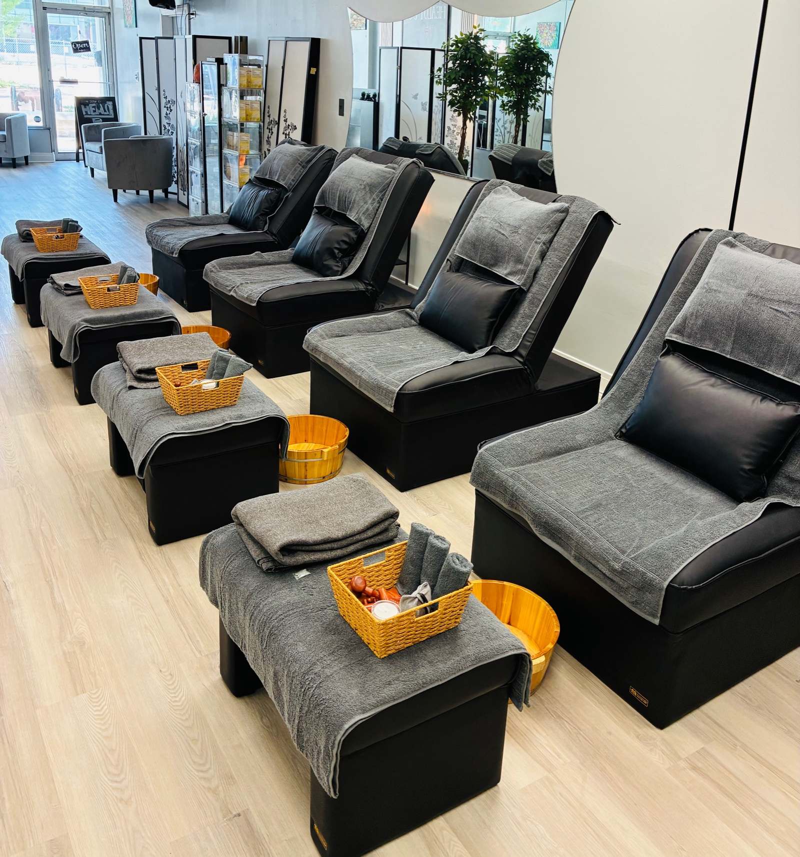 The reflexology lounge at Healot R Us: black recliners with grey towels, wooden foot basins, oak floors.